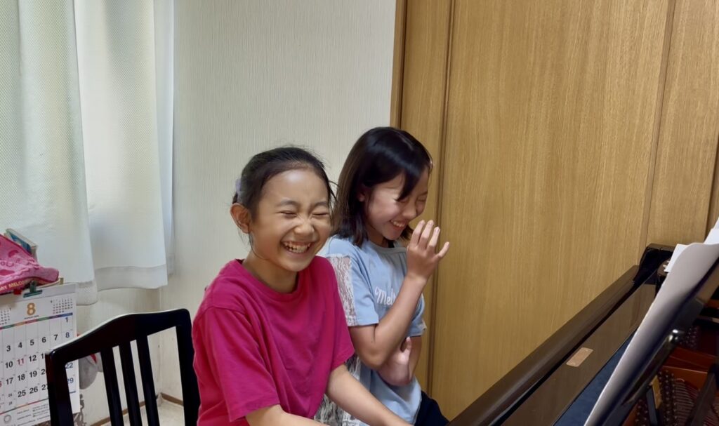 同じ学年の生徒2人が笑顔でピアノ連弾を楽しむ様子
