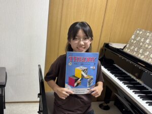 ピアノの前でセオリーのテキストを持つ生徒