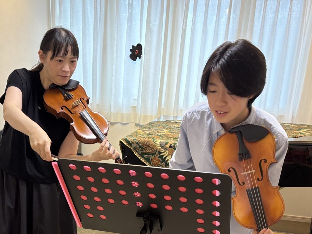 バイオリンのレッスン中に講師と中学3年生の生徒が楽譜を見ながら練習している様子
